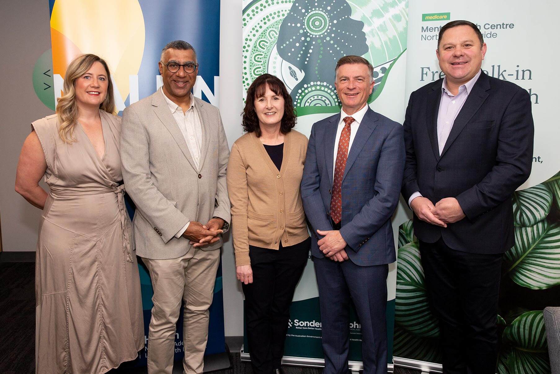 A group of five people stand together and smile in front of a banner at an event.