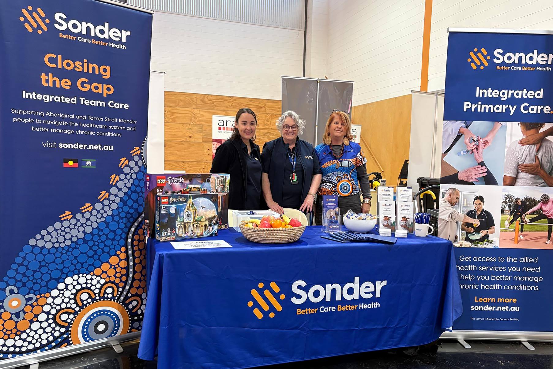 Three people stand behind a table with a Sonder banner and information brochures at a community event.