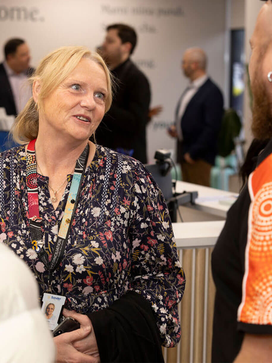 A blonde woman with a lanyard smiles while talking to someone at a professional event.