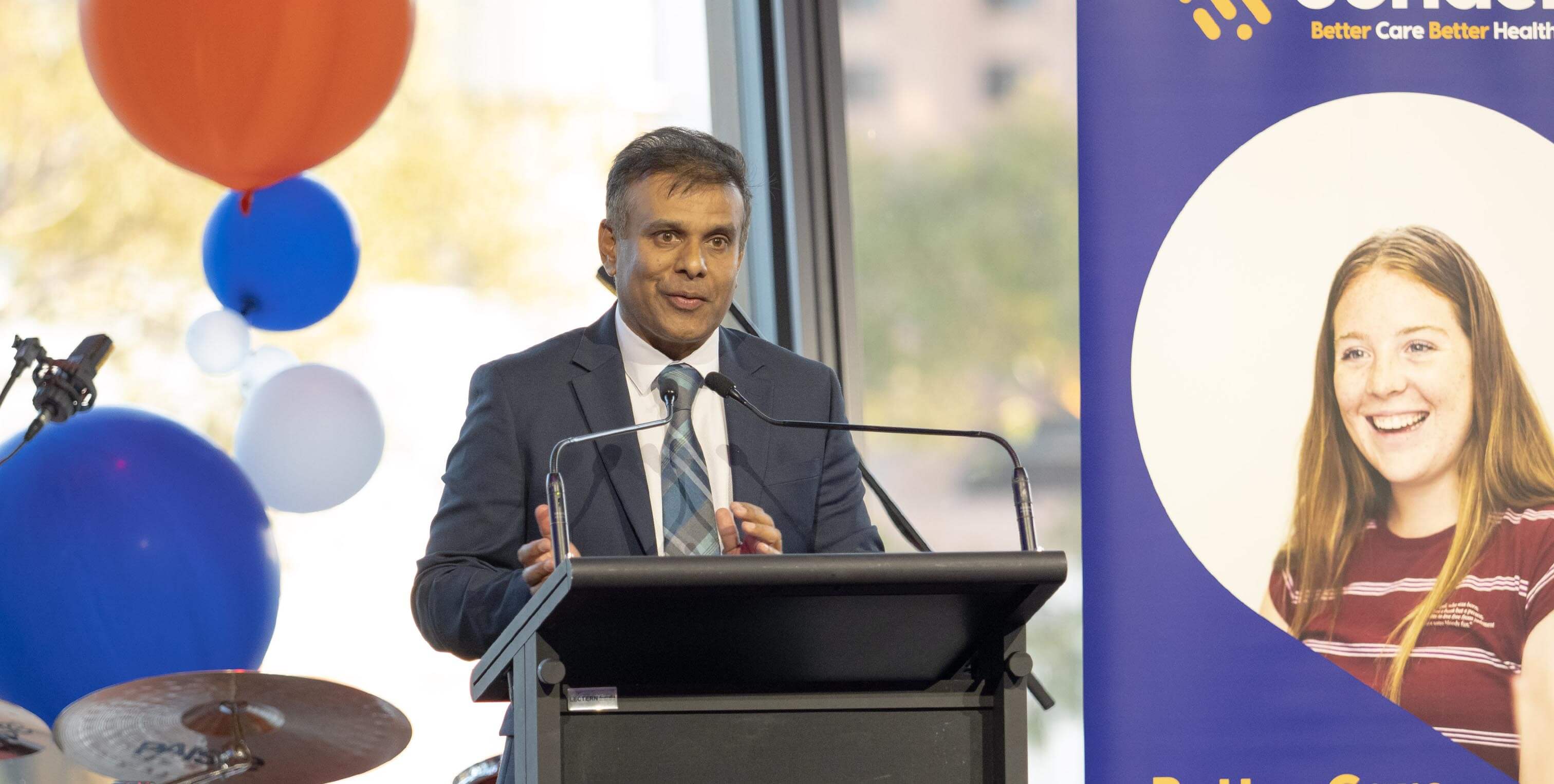 A man in a suit speaks at a podium with balloons nearby and a Sonder banner featuring a smiling girl.