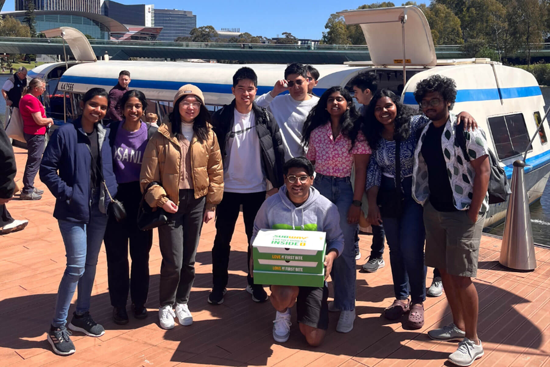 A diverse group of students stands on a dock in front of a ferry.