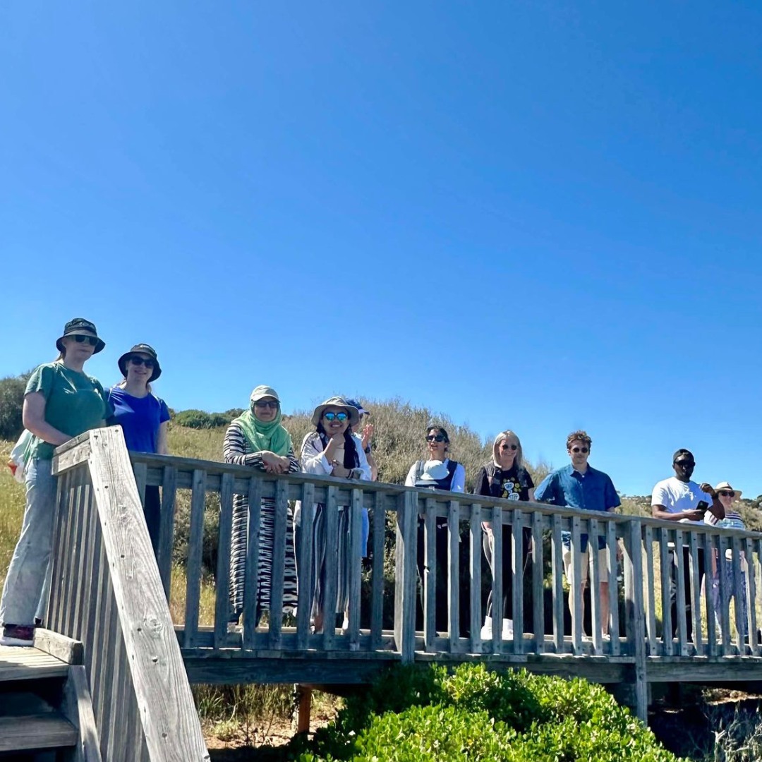A group of people stands on a wooden bridge, smiling and looking out at the viewer.